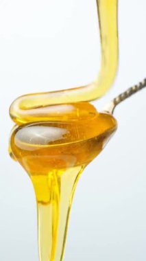Altın organik bal akışı ve metal kaşıktan damlayan beyaz bir kaşık.