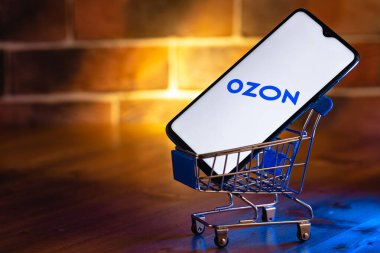 Ekran akıllı telefonunda Ozon logosu var. Yakın plan. Özon, Rusya 'daki ilk e-ticaret şirketlerinden biri. Alışveriş arabasındaki akıllı telefon..