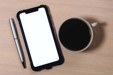 Beyaz ekranı, kalemi ve bir fincan kahveyi ahşap bir masada duran akıllı bir telefonun görüntüsü..