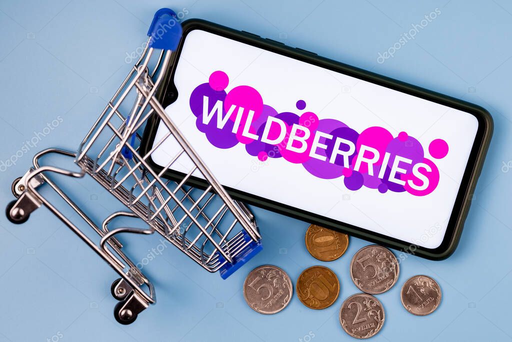 Kazan, Russia - August 23, 2021:  Wildberries is one of the largest Russian online retailer. A smartphone with the Wildberries logo on the screen, a shopping cart and ruble coins.