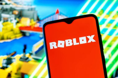 Kazan, Rusya - 25 Ağustos 2021: Roblox çevrimiçi oyun platformu ve oyun oluşturma sistemidir. Akıllı telefon ekranında Roblox logosu. Arkaplanda Roblox oyunundan bir çerçeve.