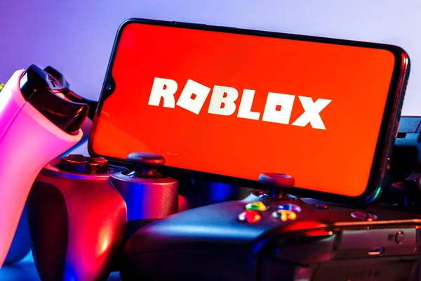 ロシアのカザン 2021年8月25日 Robloxはオンラインゲームプラットフォームとゲーム作成システムです ゲームパッドの山の画面上にRobloxロゴを持つスマートフォン — ストック写真