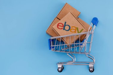 Kazan, Rusya - Sep 25, 2021: eBay online alışveriş, açık artırma ve pazar hizmetleri sunan bir e-ticaret şirketidir. Alışveriş arabasında eBay logosu olan mavi arka planda bir paket kolajı. 