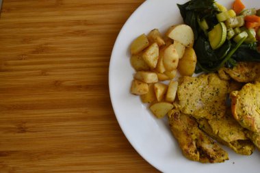 Tahta bir masada tavuk, patates ve sebze tabağı.