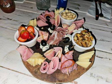 Pişmiş et, güzel peynir, taze çilek, şam fıstığı, ceviz, zeytin içeren zarif şarküteri tahtası.