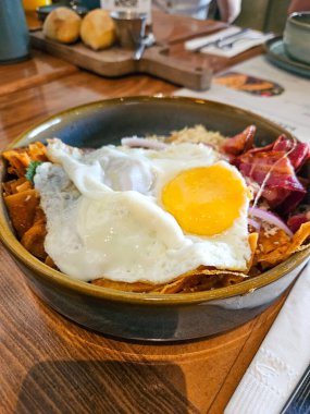 İki kızarmış yumurta, kıtır pastırma ve kırmızı soğanla süslenmiş bir kasede iştah açıcı Meksika Chilaquiles. Lezzetli ve tatmin edici bir yemek.
