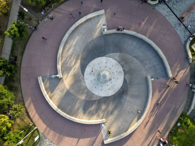 Zapopan, Meksika - 19 Ocak 2025: Spiral çeşme ve şehir meydanı yukarıdan. İnsanlar boş zamanlardan, yürümekten ve bisiklete binmekten hoşlanır. Günışığı modern mimari tasarım üzerinde uzun gölgeler bırakır.