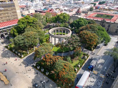 Guadalajara, Meksika - 8 Kasım 2025: Ünlü Jalisco vatandaşlarının insansız hava aracı görüşü, Guadalajara. Dairesel anıt, yeşil park, portakal ağaçları, şehir sokakları, binalar, insanlar, güneşli