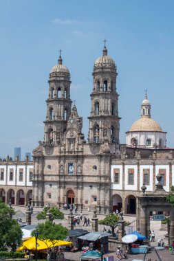 Zapopan, Meksika - 10 Ağustos 2025: Zapopan Bazilikası 'nın taş kuleler, kubbe ve aşağıdaki kamu pazarı ile dikey ön çekimi