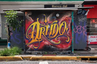 Guadalajara, Meksika 23 Ağustos 2025: Vibrant sarı ve mor graffiti şehir merkezindeki Guadalajara kaldırımında kapalı bir metal sokak büfesini süslüyor.