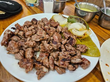 Delicious grilled diced beef, charred onions, and a roasted green pepper on a white plate. Ideal for making flavorful Mexican tacos