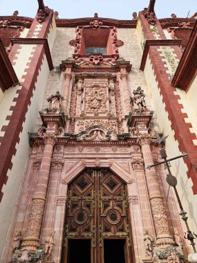 Taxco, Meksika - 21 Aralık 2024: Taxco, Meksika 'daki Santa Prisca Kilisesi' nin enfes Barok girişi. Karmaşık pembe taş oymalar, sütunlar, dini figürler ve süslü ahşap kapılar.