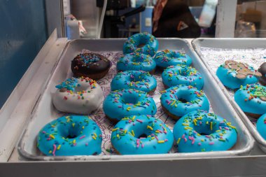 Renkli serpiştirilmiş canlı mavi donutlar, artı beyaz ve çikolata versiyonları, bir fırın vitrininde bir tepside.