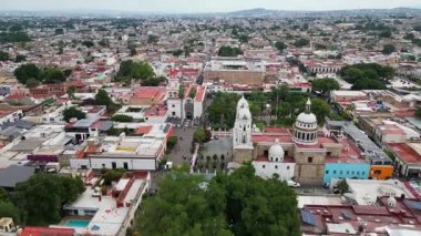 Tlaquepaque, Meksika 'nın geniş insansız hava aracı görüntüsü, tarihi şehir merkezini geleneksel mimari, ikonik tapınak ve bulutlu gökyüzü altında canlı kentsel yaşamla gözler önüne seriyor..