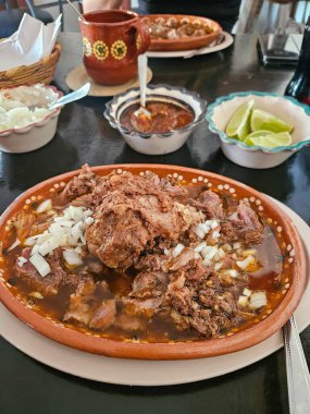 Geleneksel Meksika Birria güveci, taze doğranmış et, bol et suyu ve taze doğranmış beyaz soğan, limon ve salsa ile servis edilir.