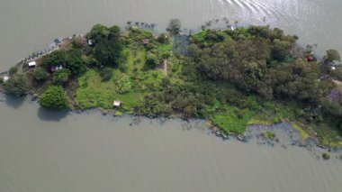 Akrep Adası 'nın insansız hava aracı görüntüsü, dağınık evleri ve kıyıları boyunca demirlemiş tekneleri olan yemyeşil bir kara parçası, sakin göl suyuyla çevrili, ince dalgalanmalar sergiliyor.