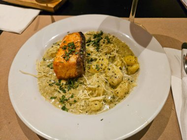 Kremalı gnocchi üzerine tavada kurutulmuş somon filetosu ile beyaz bir tabağın üstünden. Taze yeşilliklerle süslenmiş ve rendelenmiş parmesan