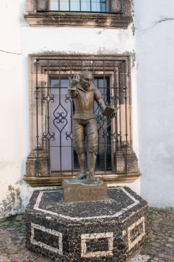 Taxco, Meksika - 21 Aralık 2024: Juan Ruiz de Alarcon onuruna yapılan bronz heykel, Taxco, Guerrero, Meksika 'da sömürge tarzı bir pencereye dayanıyor.