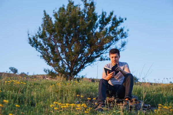 Uomo siede su una collina con un libro e pensare sul backgraound o — Foto Stock