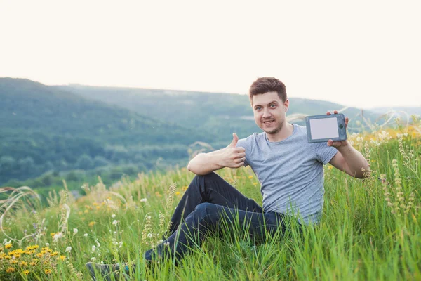 Man sits on the hill hold an eBook and keep his finger up — Stock Photo, Image