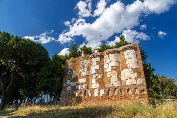 Imposing brick mausoleum of Casal Rotondo, Appia Antica. In relief marble decorations of masks, floral decorations, pieces of Roman architecture on a day of sun and clouds. Rome Roman countryside.