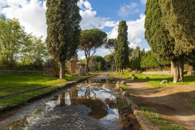 Appian Way Rome, fırtınadan sonra gökyüzü ve bulutlar, deniz çamları ve bir sonbahar gününde selvi ile birlikte mezarların kalıntılarının birikintisine yansıyor. Regina Viarum, İtalya.
