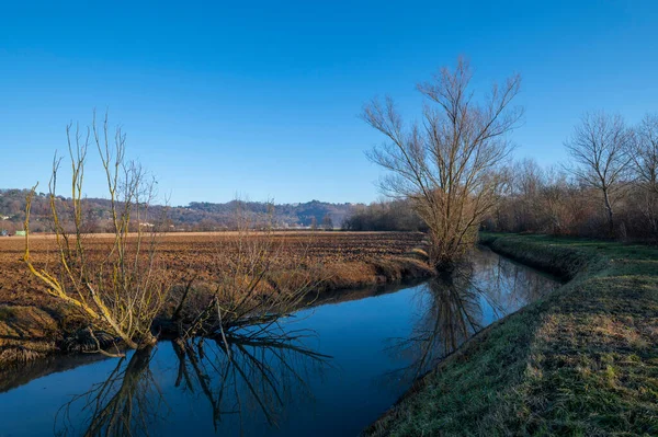 Kuzey İtalya kırsalının panoraması, nehrin ayrıntıları ve ağaçların nehirde yansıtıldığı setler soğuk bir sonbahar gününde güneşin yansımalarıyla, ama güneşle. Veneto. İtalya.