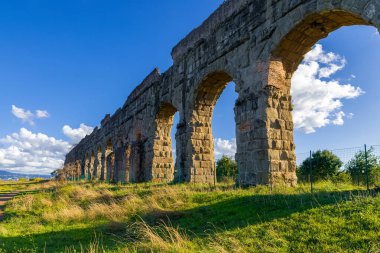 Aqueducts Roma Parkı, Claudio 'nun heybetli kemerleri mavi gökyüzü, bulutlar ve gölgeler çimlere yansıyor. Antik Roma 'nın arkeolojik su sistemi. Appia Bölgesel Parkı üzerinden İtalya.