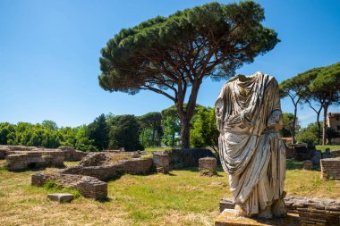 Ostia Antica, Roma İtalya. Roma 'da arkeolojik park alanındaki bir toga heykelinin ayrıntıları. İçinde imparatorluk döneminden kalma tuğla mimari binalar var. Yazın mavi çam ağaçları. İtalya..