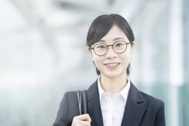 Takım elbiseli ve gülümseyen gözlüklü Asyalı genç kadın.