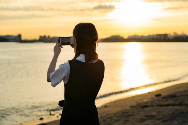 Asyalı kız lise öğrencisi akıllı telefonuyla manzara fotoğrafı çekiyor.