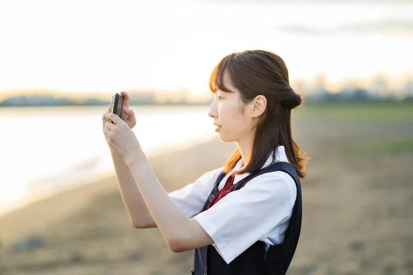 Asian female high school student taking pictures of scenery with a smartphone