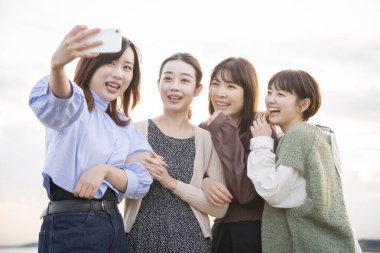 Akıllı telefonuyla hatıra fotoğrafı çeken 4 genç kadın.
