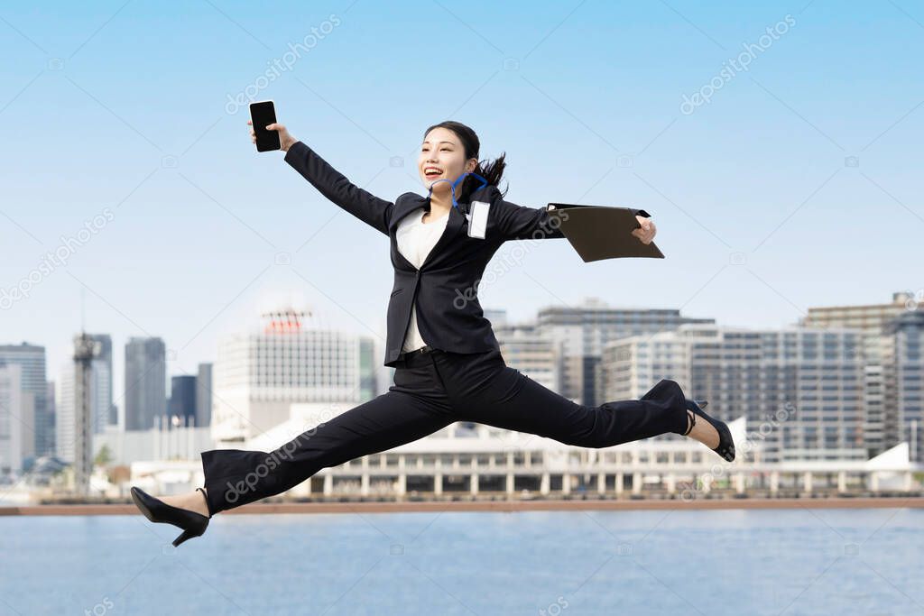 A young business woman in a suit jumping with a smile