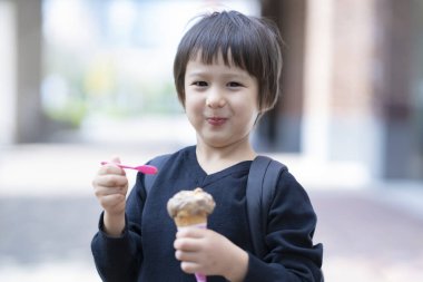 Çocuk dışarıda kaşıkla dondurma yiyor.