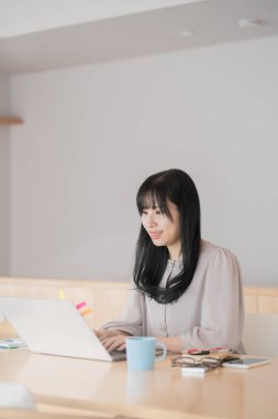 Asyalı siyah saçlı kadın evde dizüstü bilgisayar kullanarak çalışıyor.