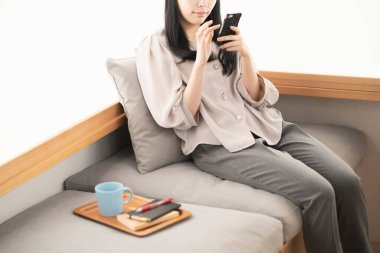 Asyalı kadın evde oturuyor ve akıllı bir telefon kullanıyor.