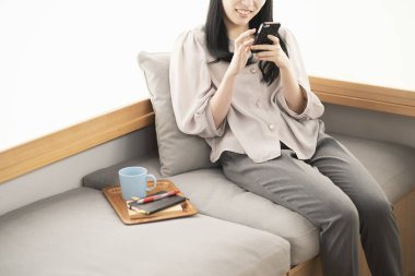 Asyalı kadın evde oturuyor ve akıllı bir telefon kullanıyor.