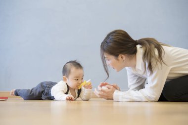 Asyalı genç anne yerde bebekle oynuyor.