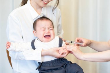 Annesi tarafından tutulurken aşı olan bir bebek.