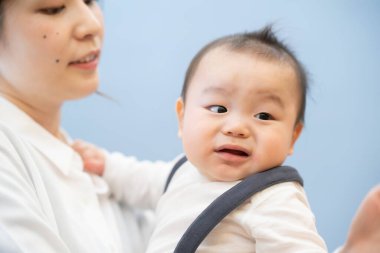 Asyalı genç anne gülümseyerek bir bebek tutuyor.