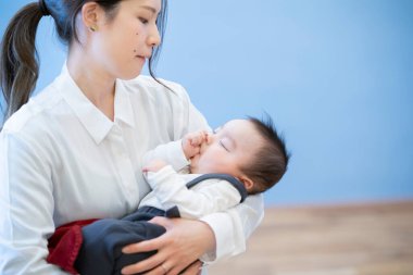 Asyalı genç anne odada uyuyan bebeğe sarılıyor.