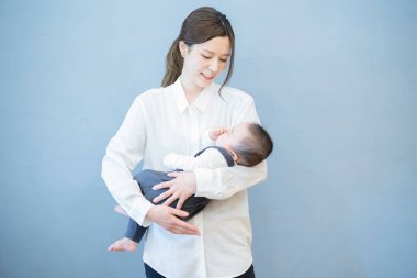 Asyalı genç anne odada uyuyan bebeğe sarılıyor.