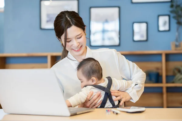 Asijské Žena Držení Dítě Provoz Notebook Indoors — Stock fotografie