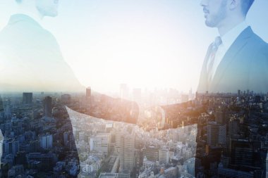 Bir iş adamının el sıkışırken çekilmiş resmi ve bir şehir.