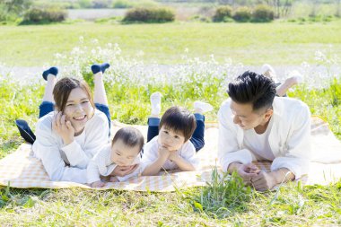 Asyalı aile yeşil alanda yan yana yatıyor.