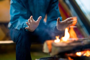 Çadırın önünde şenlik ateşinin keyfini çıkaran bir adam.