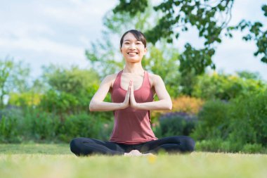 Yeşil bir parkta yoga yapan genç bir kadın.