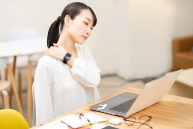 Asyalı genç bir kadın iş sırasında sert omuzları önemser.