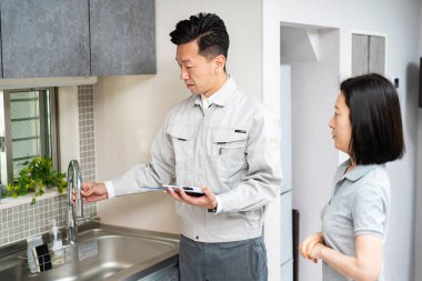 İş elbiseli bir adam mutfakta bir kadına açıklama yapıyor.) 